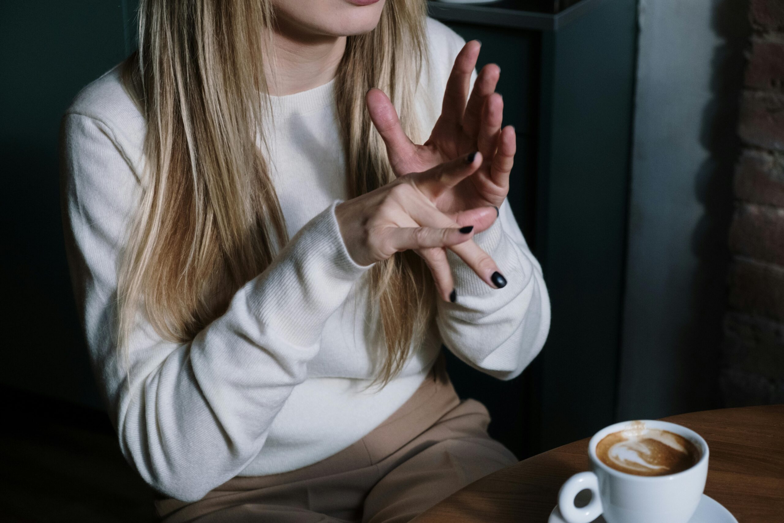 Close-up of a woman gesturing in sign language with a latte in focus, illustrating communication and lifestyle.